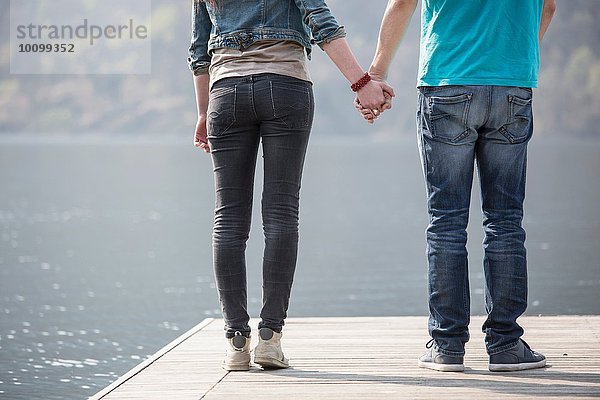 Ausschnitt aus der Rückansicht eines jungen Paares  das am Pier des Mergozzo-Sees  Verbania  Piemonte  Italien  Händchen hält.