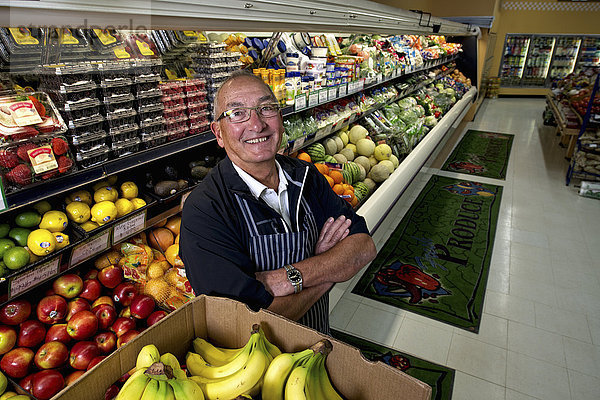 Ein Mann steht in einem Lebensmittelgeschäft neben einer Auslage mit frischem Obst und Gemüse.