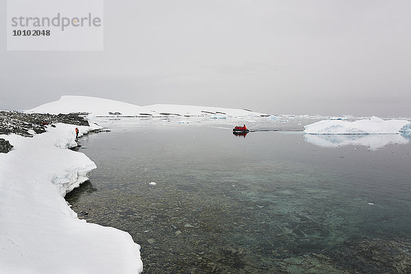 Gruppe von Menschen in einem Gummiboot  die sich im antarktischen Ozean in Richtung Küste bewegt  vorbei an einer Eisscholle.