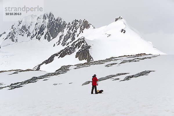 Eine Person steht auf dem Eis vor einem schneebedeckten Berg.