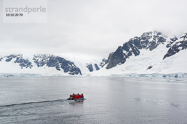 Gruppe von Menschen  die den Ozean in der Antarktis in einem Schlauchboot überqueren  im Hintergrund schneebedeckte Berge.