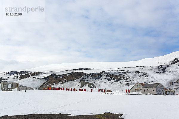Gruppe von Menschen in der Nähe einer Basis auf Deception Island  im Hintergrund schneebedeckte Berge.