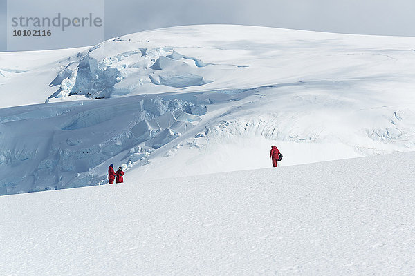 Drei Personen stehen auf dem Eis vor einem mit Eis und Schnee bedeckten Berg.