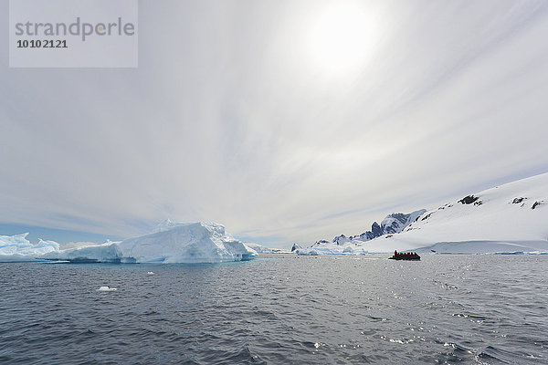 Blick auf eine Gruppe von Menschen in einem Gummiboot in der Nähe eines Eisbergs in der Antarktis.