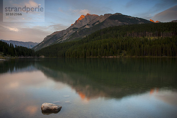 Blick über einen See auf die Berge in den kanadischen Rocky Mountains bei Sonnenuntergang.