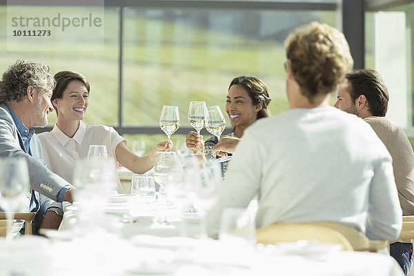 Freunde stoßen im sonnigen Restaurant auf Weingläser an.