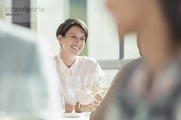 Lächelnde Frau trinkt Weißwein im sonnigen Restaurant