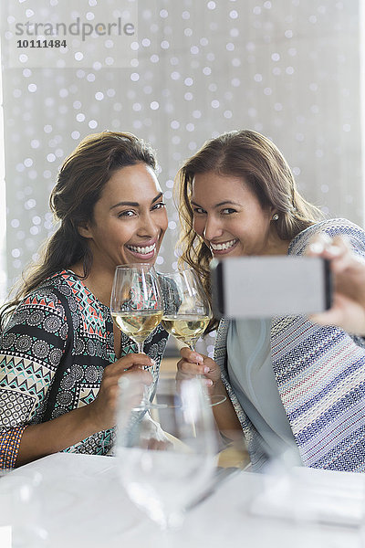 Frauen mit Weißwein nehmen Selfie mit Fotohandy im Restaurant