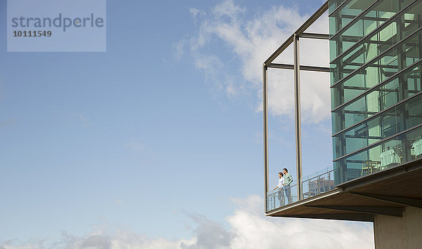 Männer  die auf einem Balkon aus Glas stehen  stoßen gegen den blauen Himmel.