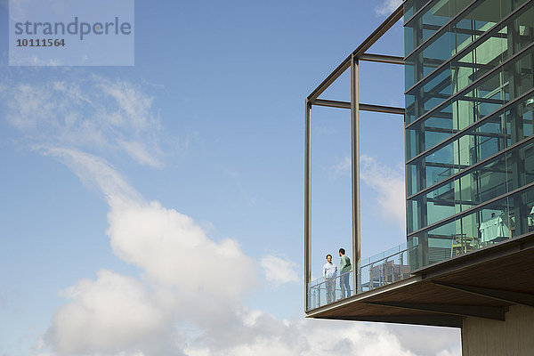 Männer  die auf dem Balkon aus Glas reden  stoßen gegen den blauen Himmel.
