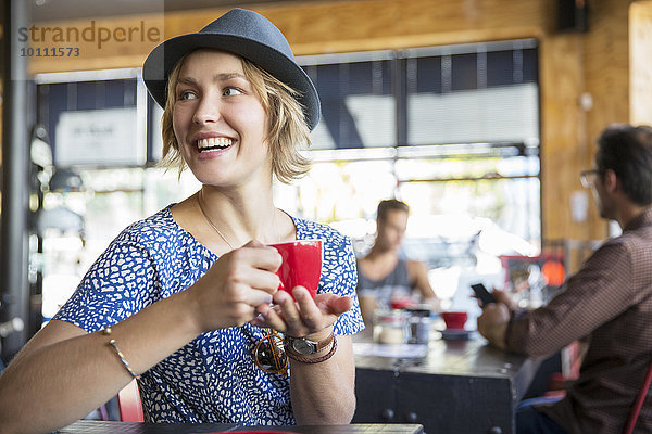Lächelnde Frau trinkt Kaffee und schaut im Cafe über die Schulter