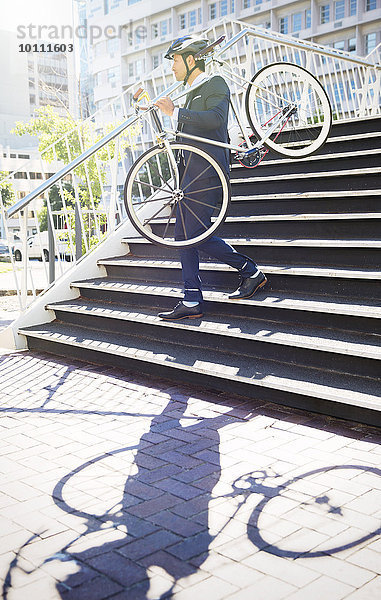 Geschäftsmann im Anzug und Helm mit Fahrrad über die Stadttreppe