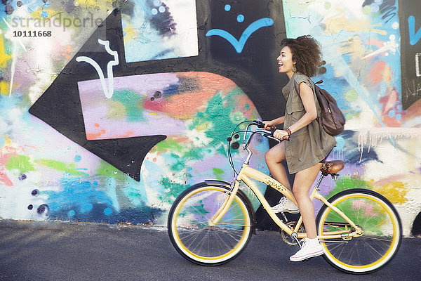 Frau fährt mit dem Fahrrad an einer mehrfarbigen Graffiti-Wand entlang