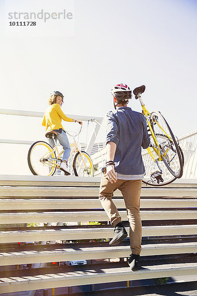 Mann im Helm trägt Fahrrad die Stadttreppe hinauf