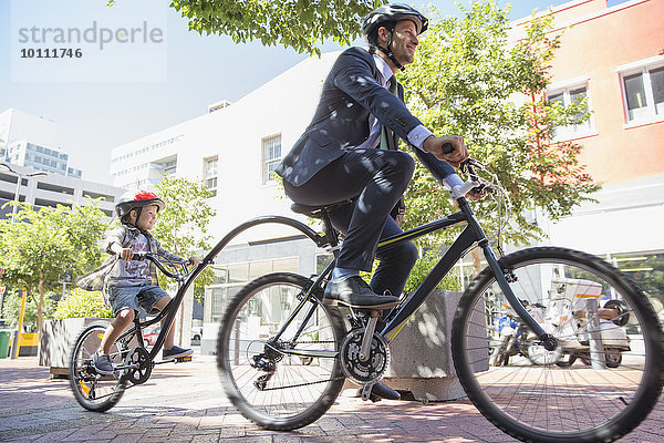 Geschäftsmann Vater im Anzug fährt Tandemfahrrad mit Sohn auf städtischem Bürgersteig