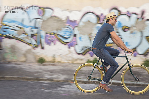 Hipster-Mann beim Radfahren auf der Straße entlang der städtischen Graffiti-Wand