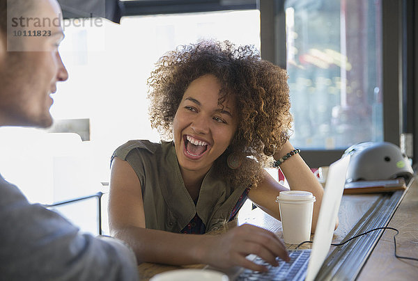 Enthusiastische Frau lacht über Laptop im Cafe