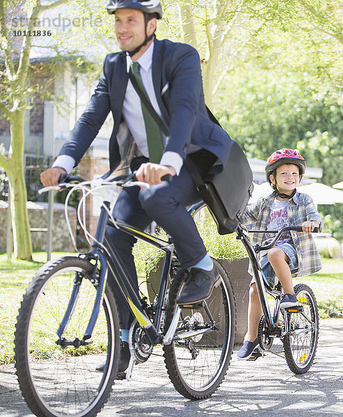 Geschäftsmann in Anzug und Helm auf Tandemfahrrad mit Sohn