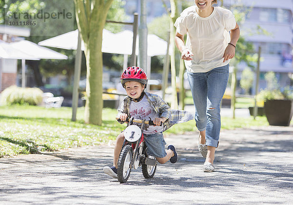 Mutter jagt Sohn auf dem Fahrrad mit Helm im sonnigen Park