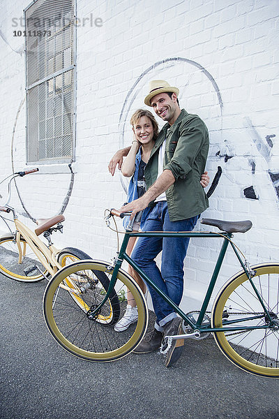 Porträt eines lächelnden Paares mit Fahrrädern an der Stadtmauer