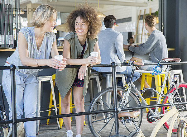 Lächelnde Freunde beim Kaffeetrinken auf der Caféterrasse beim Fahrradfahren