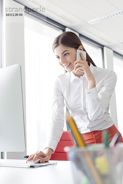 Geschäftsfrau beim Telefonieren am Computer im Büro
