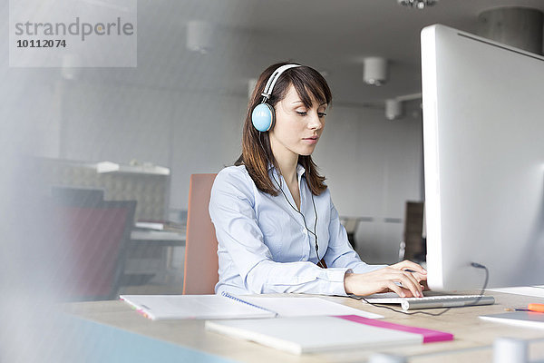 Braune Geschäftsfrau mit Kopfhörer am Computer im Büro