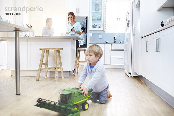 Frauen kochen in der Küche  während der Junge mit dem Spielzeugtraktor auf dem Boden spielt.