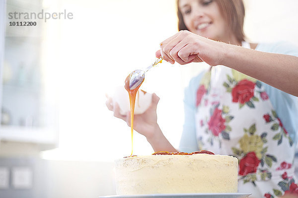 Frau gießt Karamell über Kuchenbacken in der Küche