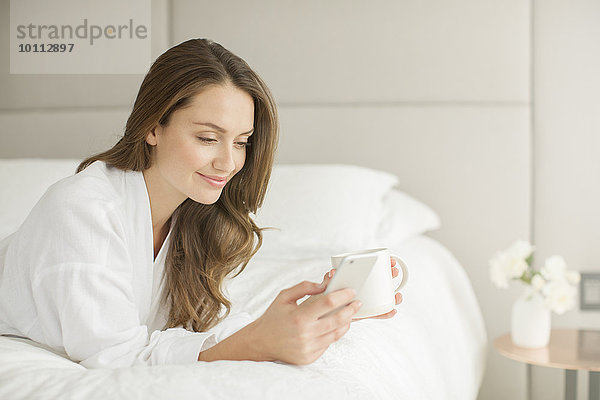 Handy Frau Kurznachricht lächeln Bett Bademantel trinken Kaffee