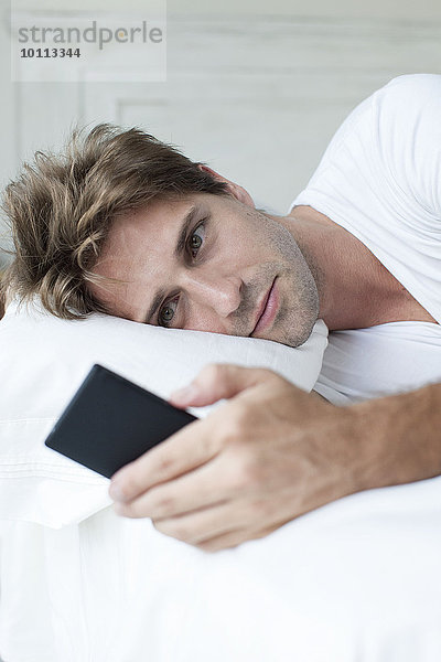 Mann im Bett liegend mit Smartphone