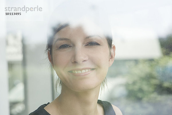 Frau schaut durchs Fenster  lächelnd  Portrait