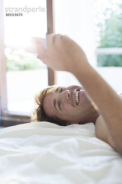 Mann im Bett liegend mit Multimedia-Smartphone für Instant Messaging