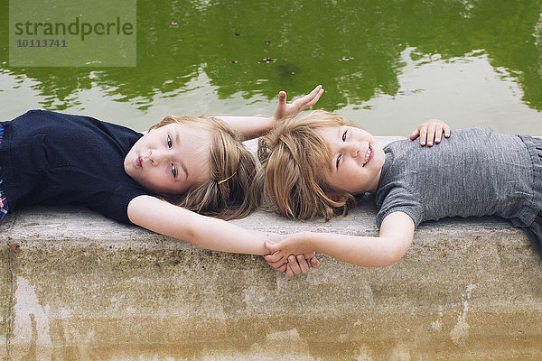 Kleine Mädchen  die zusammen am Teich liegen und Händchen halten.