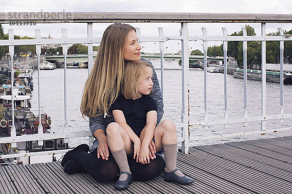 Mutter und Tochter sitzen zusammen auf der Brücke über den Kanal.