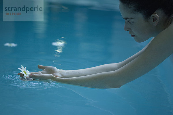 Frau  die nach einer Blume greift  die im Pool schwimmt.