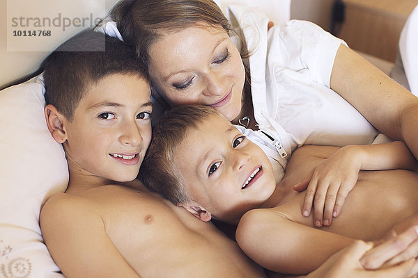 Mutter und kleine Söhne entspannen gemeinsam auf dem Bett  Porträt