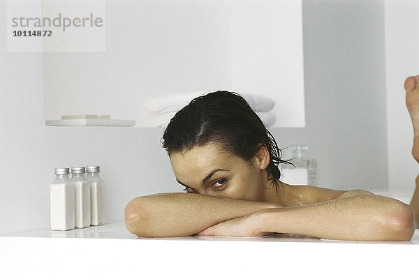 Frau in der Badewanne  Kopf auf den Armen ruhend  Blick in die Kamera