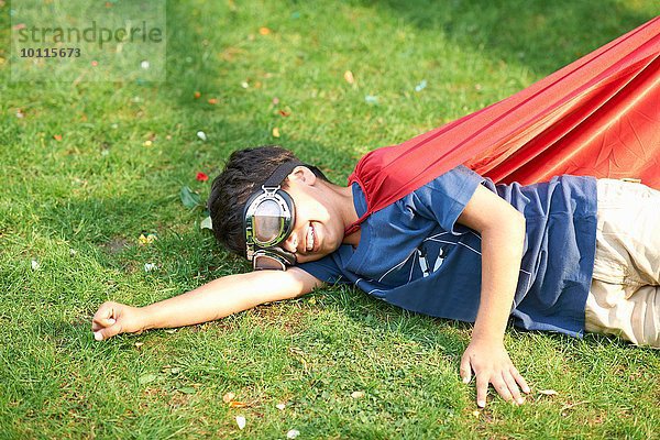 Junge mit Brille und Umhang seitlich auf Gras liegend  fliegende Haltung