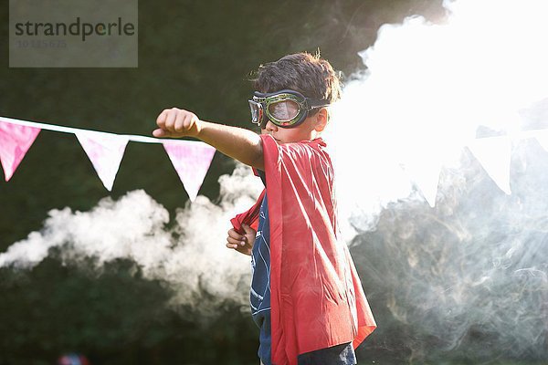 Junge mit Brille und Umhang in Superheldenhaltung vor Rauchwolke