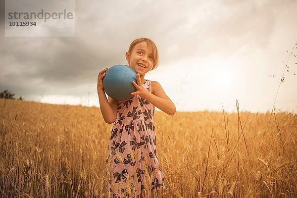 Mädchen mit blauer Kugel im Weizenfeld