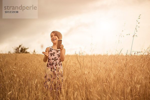 Mädchen mit Smartphone beim Lachen im Weizenfeld