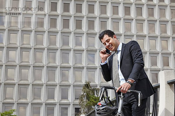 Mittlerer Erwachsener Geschäftsmann  der ein Fahrrad hält und mit dem Smartphone telefoniert.