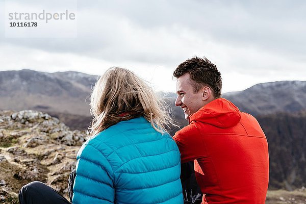 Junges Paar auf einem Hügel sitzend  Rückansicht  Keswick  Lake District  Cumbria  Großbritannien