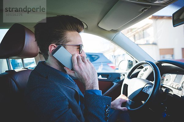 Stilvoller junger Mann beim Autofahren auf dem Smartphone