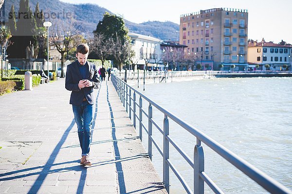 Junger Mann beim Bummeln und Lesen von Smartphone-Texten am Seeufer  Rovato  Brescia  Italien