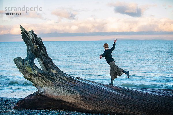 Frau auf großem Treibholzbaumstamm am Strand stehend