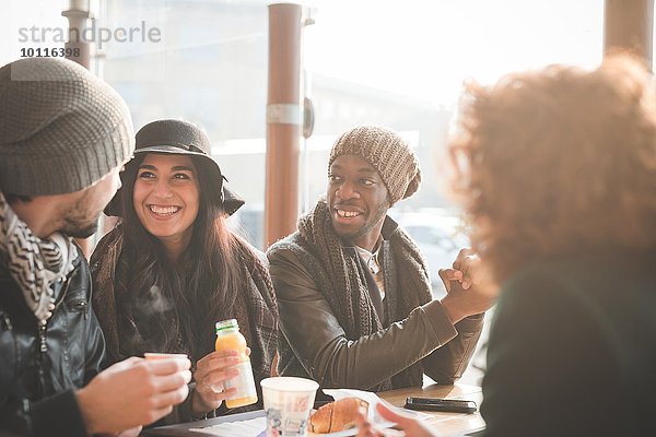 Vier junge erwachsene Freunde beim Plaudern im Straßencafé