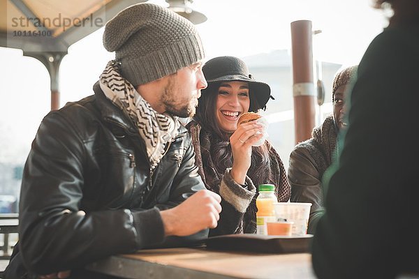 Vier junge erwachsene Freunde beim Plaudern und Donuts essen im Straßencafé