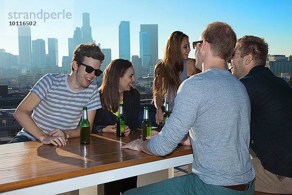 Sechs erwachsene Freunde reden und trinken Bier an der Dachbar mit Skyline von Los Angeles  USA